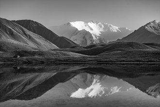 White glaciated and snowy mountain peak Lenin Peak at sunset, mountains reflected in a lake between