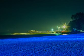 Night scene at beach soft blue light with pier lit up by street lights in background