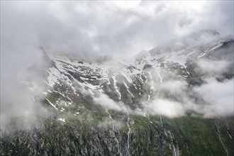 Snow-covered cloudy mountains with summit Hochsteller, mountain streams as waterfalls on a