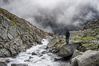 Mountaineer at a mountain stream, Furtschaglbach, cloudy mountains in the background,