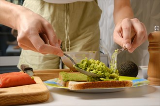 Closeup view of hands of woman spreading mashed avocado on toast