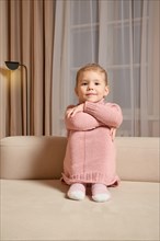 Cute little girl sitting on the sofa with her pink sweater pulled over her knees