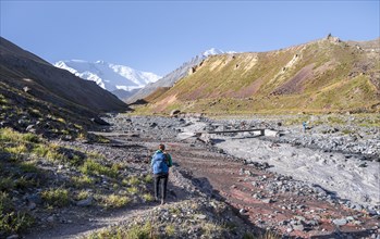 Hiker iTal with river Achik Tash between high mountains, mountain landscape with peak Pik Lenin,