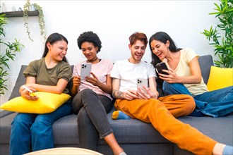 Frontal view of multi-ethnic friends using mobile sitting on the sofa at home
