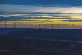 Row of wind turbines on the horizon under a colourful evening sky, open-cast lignite mine, North