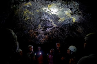 A group of people in helmets listen to a guide in the lava tunnel Gruta das Torres, Gruta das