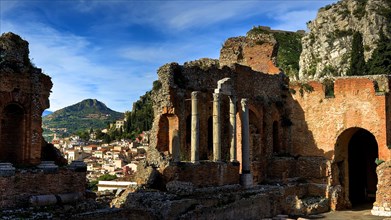 Ancient amphitheatre, ancient columns and ruins overlooking a town and surrounding mountains,