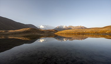 White glaciated and snowy mountain peak Pik Lenin at sunrise, mountains reflected in a lake between