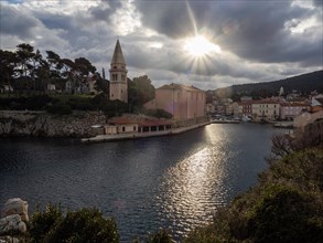 Morning sun breaking through clouds, view of the harbour entrance of Veli Losinj, with St.