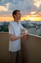 Man in white polo shirt standing on balcony in dusk
