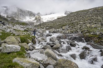 Mountaineers at a mountain stream, behind them rocky mountains with glacier Furtschaglkees,