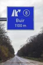 A traffic sign with a directional arrow points to the Buir motorway exit under a blue sky,