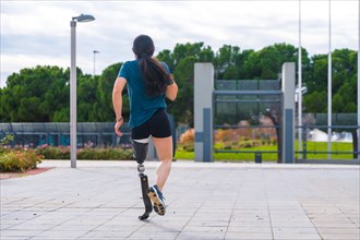 Rear view of a handicapped runner with a prosthetic leg in a park