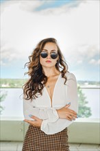 Outdoor portrait of arrogant woman in sunglasses with folded arms