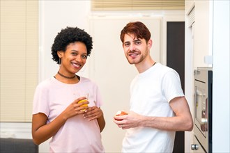 Multi-ethnic friends standing in the kitchen having healthy breakfast looking and smiling at camera