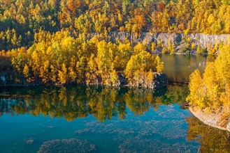Autumn landscape with colourful trees on the shore of a lake next to a steep cliff, former
