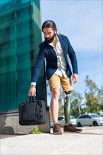 Vertical photo of a businessman with prosthetic leg leaving a laptop bag on the floor outdoors