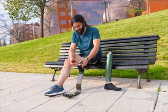 Physically disabled man adjusting prosthetic leg before running sitting on an urban park bench