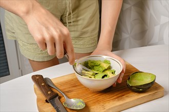 Unrecognizable woman mashes avocado pulp with a fork in a bowl