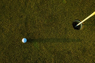 Golf Ball on the Grass with Shadow and Hole with Flag Pole on Putting Green on Golf Course in