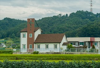 House displaying large Christian cross on roof next to rice paddy in rural farming community