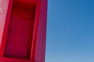 Closeup of door on red lighthouse with blue sky in background