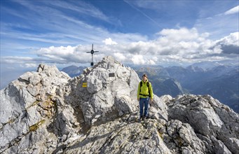 Mountaineer on the rocky summit of the Watzmann Mittelspitze with summit cross, Berchtesgaden