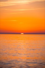 Intense, atmospheric sunset with bright orange-yellow sky over the Baltic Sea, only a small part of