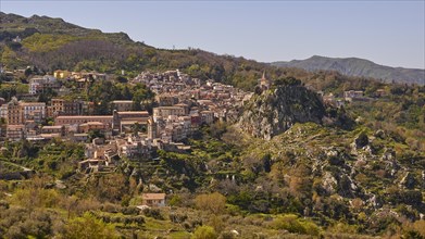 View of a town in the middle of a mountainous landscape with dense vegetation. Novara di Sicilia,