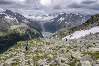 Two mountaineers on hiking trail, view of Schlegeisspeicher, glaciated rocky mountain peaks Hoher