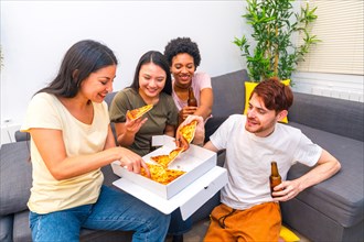 Multi-ethnic flatmates enjoying pizza and beer at home sitting on the sofa