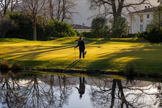 Female Golfer Reflected and Searching For Golf Balls in Water Pond on Golf Course in Switzerland