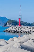 Red lighthouse on concrete pier in small coastal fishing port