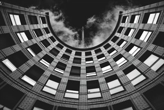 View upwards to a circular building in black and white with sky and clouds in the background,