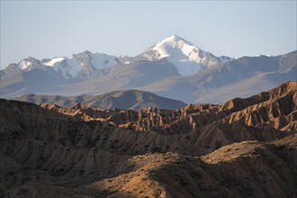 Sunrise over canyons, Tian Shan mountains in the background, eroded hilly landscape, badlands,