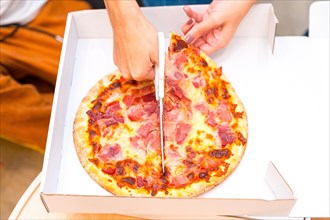 Close-up top view of an unrecognizable woman cutting pizza with scissors at home