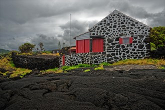 White house with red details stands on a black lava landscape under a grey sky, North Coast, Santa