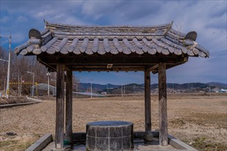 Covered water well under ceramic tiled roof full of water in a mountainside public park with plowed