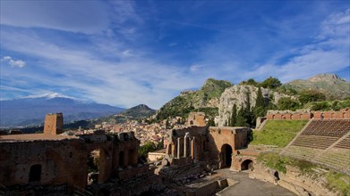 Ancient amphitheatre with ruins in front of a city silhouette and Mount Etna in the background,
