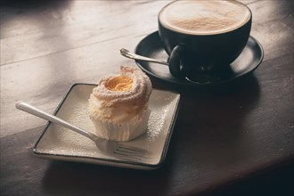 A frothy coffee served with a delicate brazo de mercedes cupcake in a cozy autumn ambiance