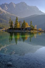 Reflection of an island in a mountain lake in front of steep mountains, autumn, evening light,