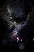 Cave explorers in the lava tunnel Gruta das Torres with helmets looking at an illuminated rock face