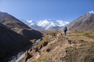 Hiker at the valley with river Achik Tash between high mountains, mountain landscape with peak Pik