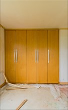 Wooden doors with metal handles of built-in closets in bedroom with debris and trash on floor in