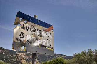 Weathered road sign with bullet holes against a blue sky and trees in the background, Anopolis,