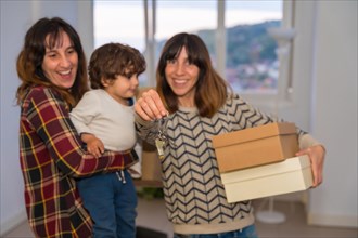 Lesbian couple and kid holding the keys of a new house carrying boxes