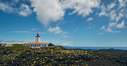 Wide lava flow with the striking lighthouse Farol da Ponta da Iha in front of a blue sky with white