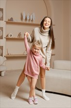 A mother and her young daughter laughing while playing together at home. They both wear knitted