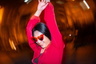 Night photo with flash and motion of fashionable woman with heart shape sunglasses dancing in the