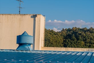 Round cone shaped exhaust vent on top of blue metal roof in front of white concrete building